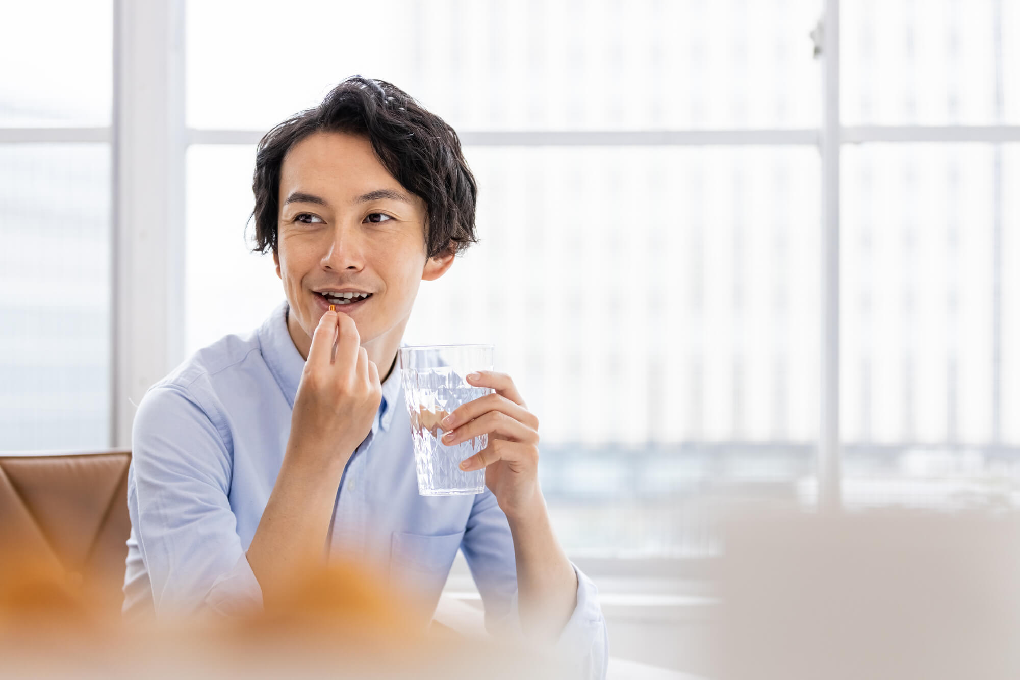 片手に水を持ち、サプリメントを飲もうとする男性