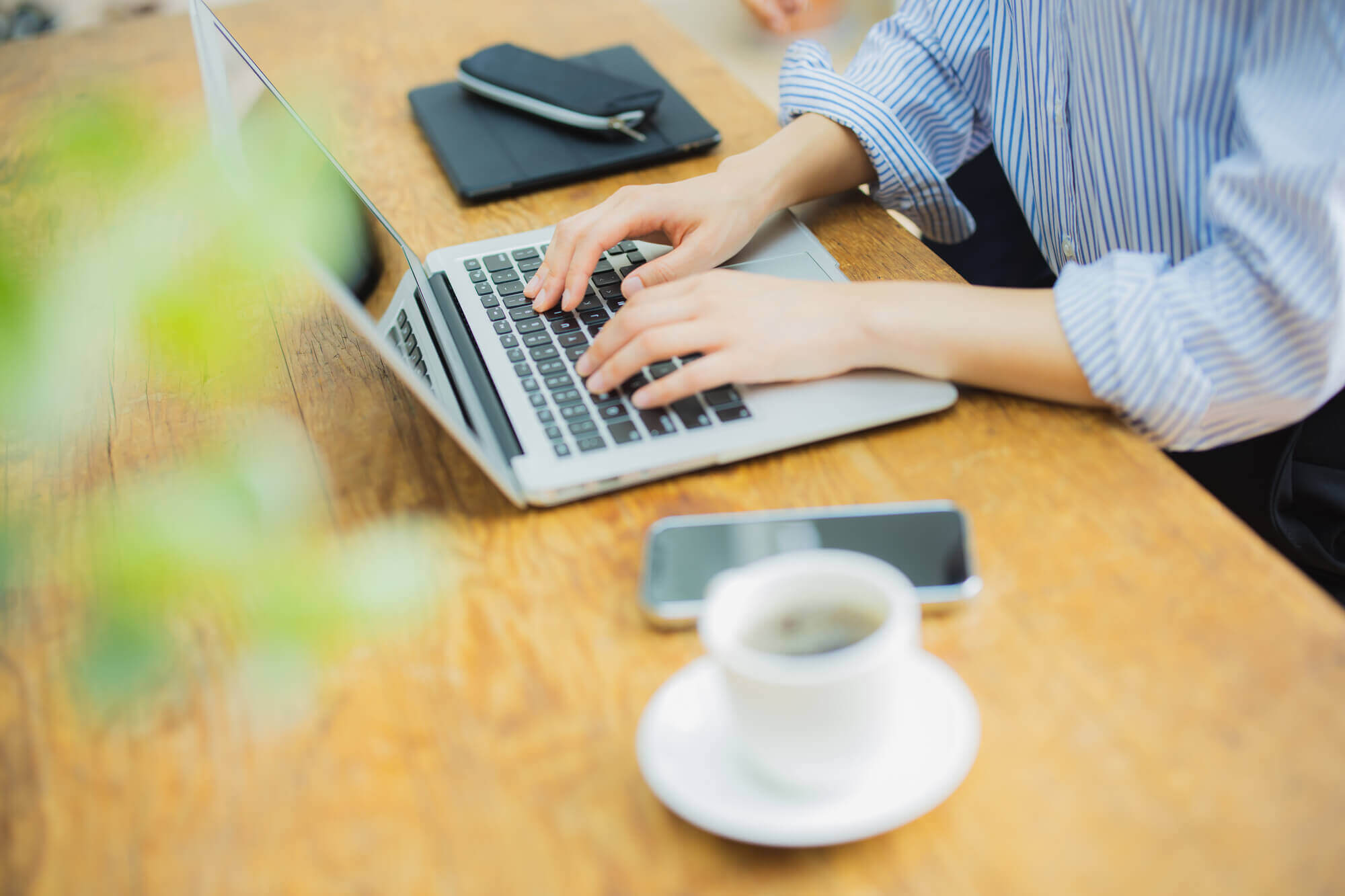 コーヒーをデスクに置いてパソコン作業する人の手