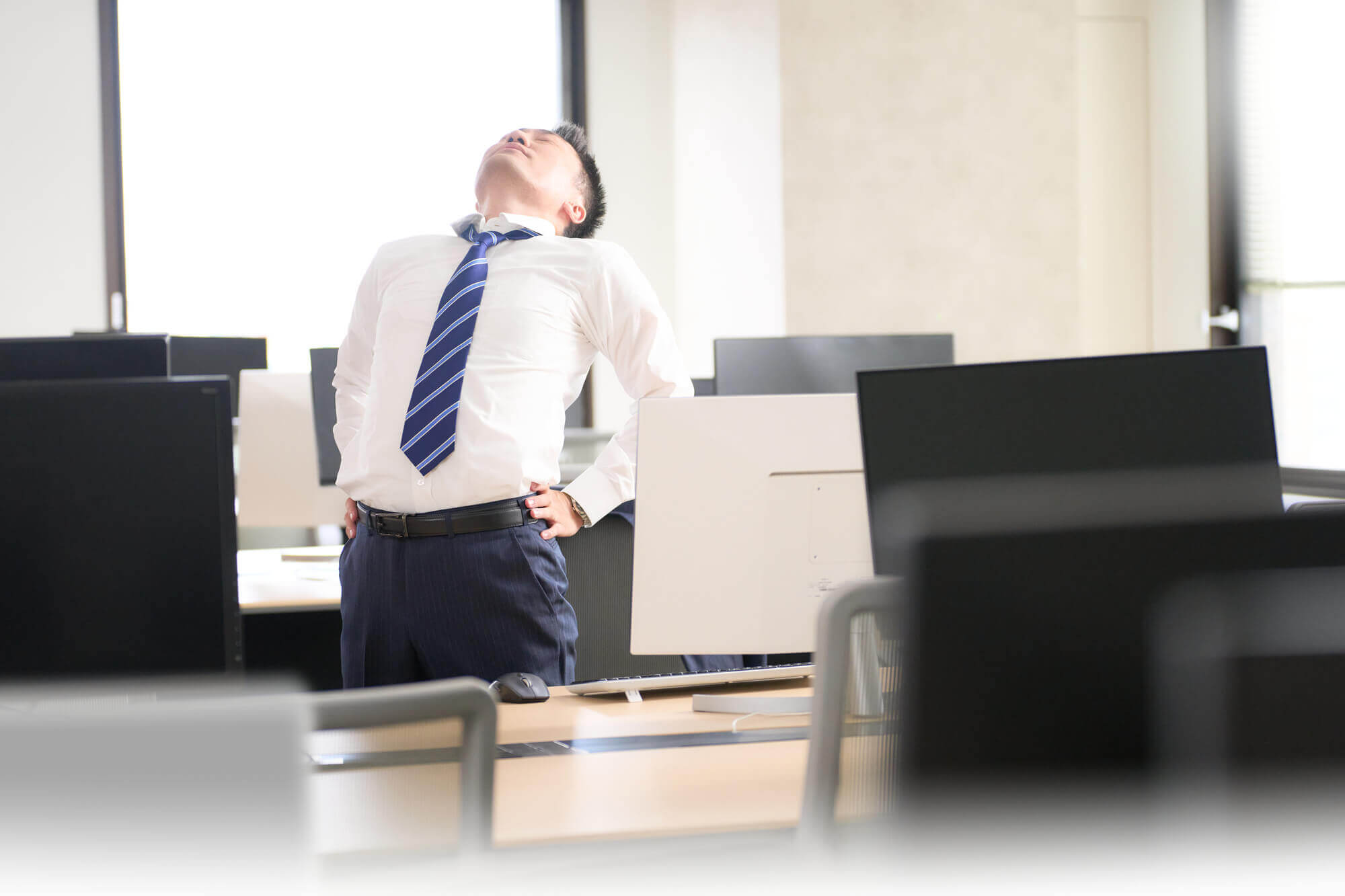 オフィスで立ち上がり、腰を伸ばす男性