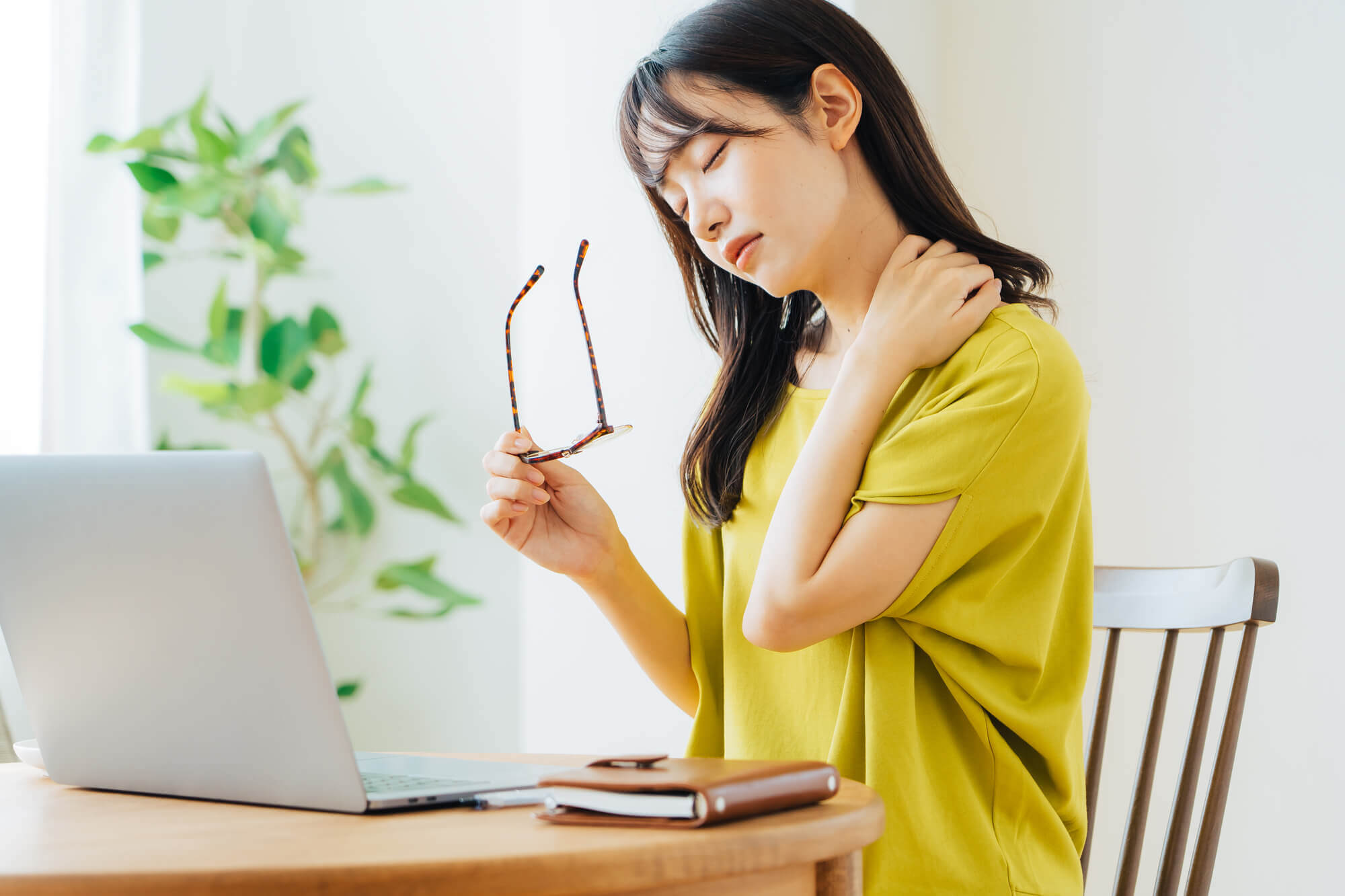 パソコンの前に座り自分の肩をもんでいる女性